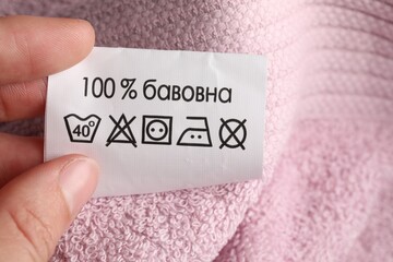 Woman holding clothing label on pink fluffy towel, closeup