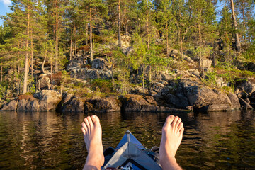 View from the lake and forest. Men's legs lie on the bow of a blue kayak