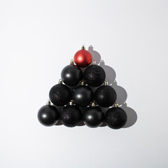 Red and black Christmas baubles stacked in shape of Christmas tree on white background. Minimal greeting concept.