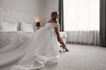 the morning of the bride. a blonde in a white dress puts on sandals.