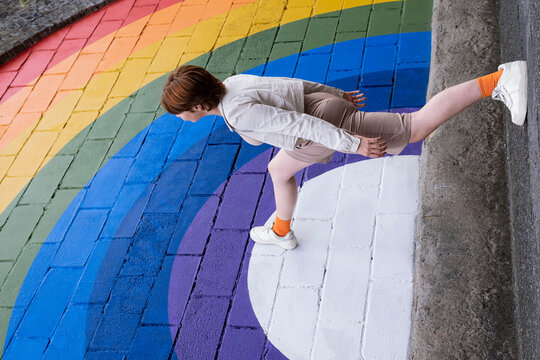 Young woman stepping on rainbow colored wall