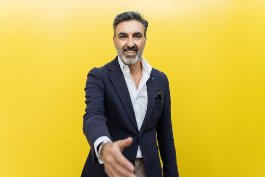 Smiling businessman doing handshake against yellow wall