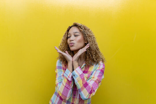 Young woman puckering with eyes closed against yellow background
