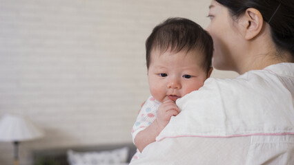 close up lovely little baby is leaning on her mother’s shoulder with cloth while being burped...