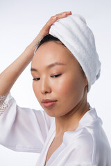 Closeup of asian womanin white gown with towel on head. Young girl posing with her arms at face. Neutral natural pink manicure on nails. Woman on white background smile.