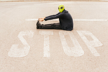 Man wearing alien mask sitting in front of STOP sign on road