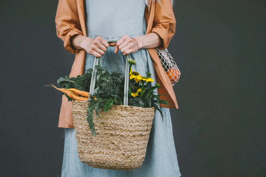 Woman holding plastic free bag with vegetables and flowers against gray background