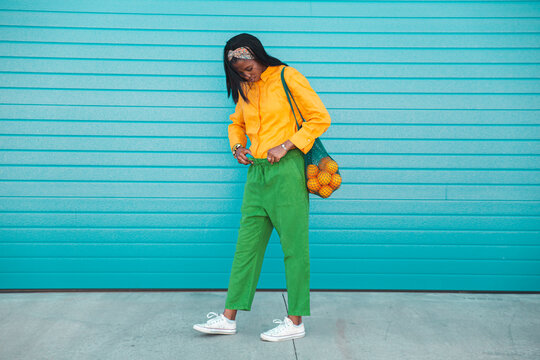 Woman carrying oranges in mesh bag by blue wall