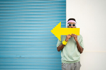 Man holding yellow arrow sign in front of lips by blue shutter