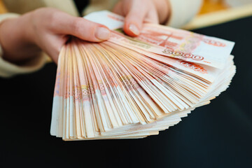 a woman holds in hands a fan of banknotes of 5000 rubles on a black background. 