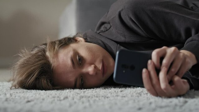 Caucasian sad woman using mobile phone and lying down on carpet. Shot with RED helium camera in 8K.    