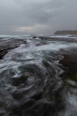 Cloudy view of the rocky coastline with high tide water flowing.