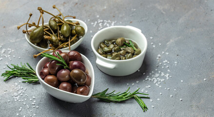 Marinated Green and Kalamata Olives and Capers with fresh rosemary in a small bowl, on light wooden background. Long banner format. top view