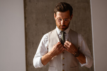 Elegant businessman in eyeglasses adjusting vest in office 