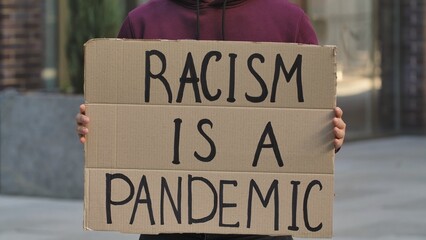 RACISM IS A PANDEMIC on cardboard poster in hands of male protester activist. Stop Racism concept, No Racism. Rallies against racism and police brutality. Peaceful life of blacks matters. Close up.