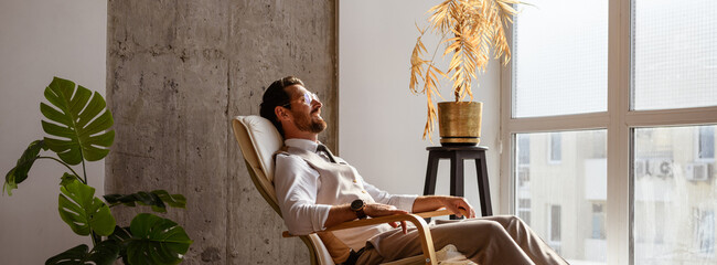 Banner view of positive ceo in eyeglasses and formal wear resting on armchair in office