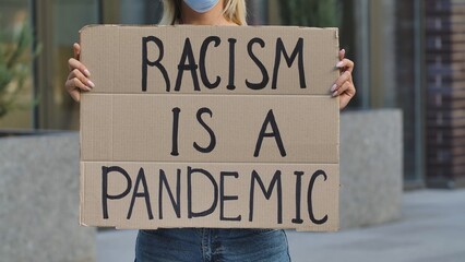 RACISM IS A PANDEMIC on cardboard poster in hands of female protester activist. Stop Racism...