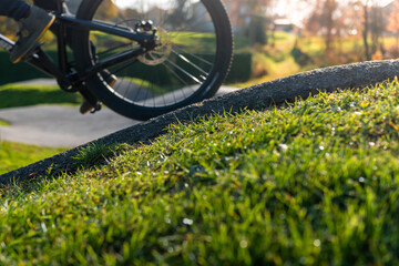 Bicycle wheel on asphalt pump track surrounded by grass and nature on a sunny day.