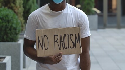 NO RACISM on cardboard poster in hands of African American male protester activist. Stop Racism...
