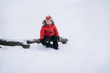 cute little caucasian boy wearing winter clothes sitting on log looking aside