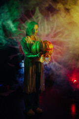 Young woman holds pumpkin in her hands and portrays bloodthirsty zombie with horror wounds and...