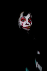 Portrait of young woman in image bloodthirsty zombie with wounds against black background.
