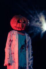 Young woman holds pumpkin on her head and portrays bloodthirsty zombie with bloody clothes.