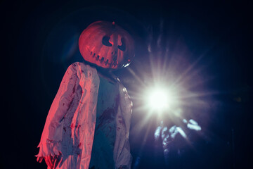 Young woman holds pumpkin on her head and portrays bloodthirsty zombie with bloody clothes.