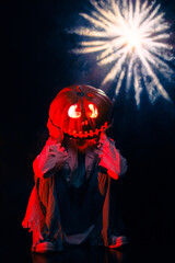 Young woman holds jack o lantern from pumpkin on her head against dark background with backlight.
