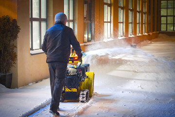 Man with track drive snow blower machine removing deep snow at night, snothrower assistant for snow...