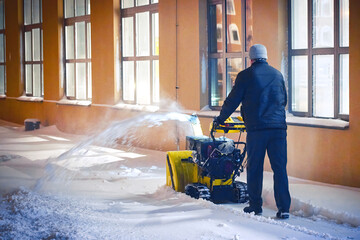 Man with snow blower remove deep snow at night, clear snowy sidewalk after blizzard, worker with snowthrower clear snow and ice in winter season. Motor snowblower removing deep snow