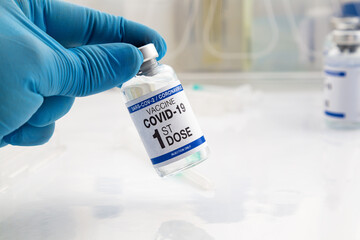 Hand holding COVID-19 Vaccine Vial for vaccination tagged with 1st dose vaccine. Doctor holding...
