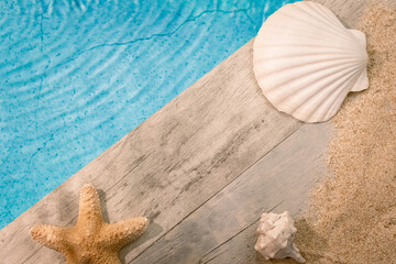 Fototapeta na wymiar Coquillages vus du dessus sur un dallage en bois au dessus d'une piscine avec une étoile de mer. Ambiance vacances en été.