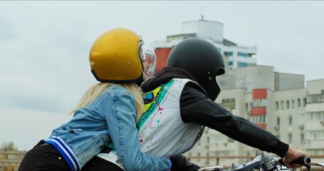 A young stylish couple of bikers meet and hug near a motorcycle standing in a public city parking lot