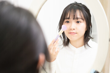 鏡の前に座ってメイクをしている若い女性