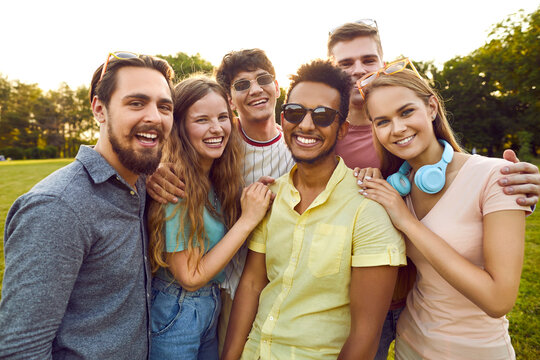 Bunch of happy young diverse people meet up, enjoy summer and have fun together. Group portrait of cheerful beautiful multi ethnic friends standing in the park, looking at the camera and smiling