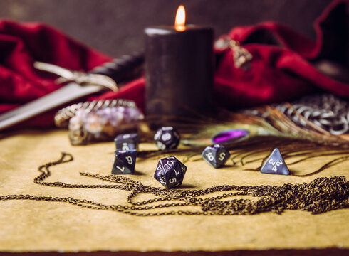 Fantasy role play board game still life concept. Selective focus on dice. Background decorated with various character objects tools. Dagger, chain mail, clothing, dice set: D10, D20, D12, D6, D8.