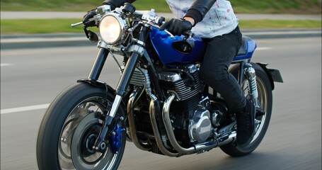 Close-up of a motorcycle riding on a road at high speed. Side view. Driving Bike on Streets. Speed Motion in Cityscape. Fast TRACKING Shot of a biker riding his custom built cafe racer through city.