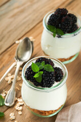 Yogurt with granola, blackberry berry fruits and muesli served in glass jar on wooden background....