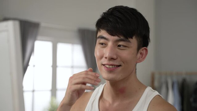 closeup shot of a confident asian young man is looking at himself in the mirror and touching his perfect face skin with a satisfied smile in the morning at home