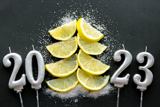 christmas fir tree from orange lemon or kiwi slices sugar instead of snow and number 2023 happy new year candles.bokeh gold light white plate black blue background.sun light on top like star.slices