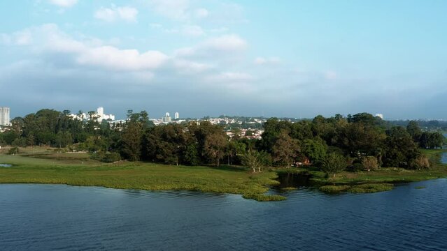 Aerial drone dolly-in rising shot of the Interlagos neighborhood in the south of S&atilde;o Paulo, Brazil from the man-made Guarapiranga Reservoir with calm waters, trees, and houses on a fall evening