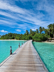 Ein Holzsteg als Bootsanleger und Jetty auf den Malediven mit Palmen und Strand im Hintergrund...