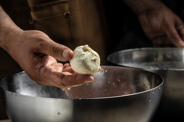A man working in a small family creamery is processing the final steps of making a cheese. Italian hard cheese silano or caciocavallo, mozzarella