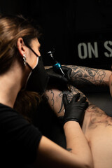Vertical photo of a woman with mask tattooing a man in a tattoo studio