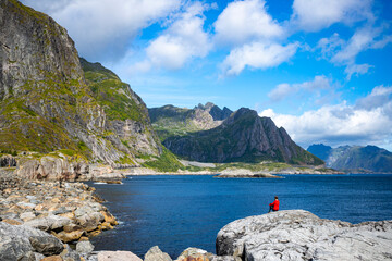 A beautiful girl sits on the rocks above the sea overlooking the mighty mountains on the lofoten...