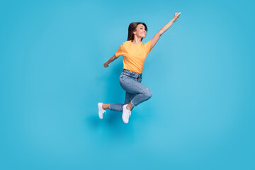 Full length photo of excited cool lady wear yellow t-shirt jumping high rising fist isolated blue color background
