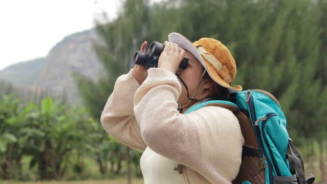 cute fat asian woman Wear a hat and carry a backpack. Holding a binoculars to watch the birds in the hill forest. nature tourism concept, traveler, trekking