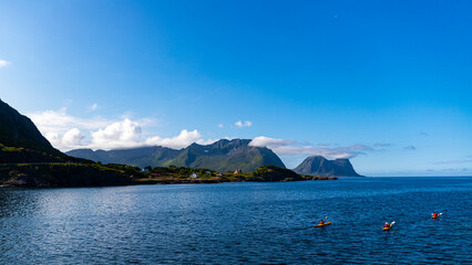 A group of sea kayakers cruise the sea on the island of senja, norway; small houses by the sea with big mountains behind them