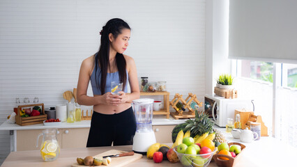 Fit and healthy young Asian woman in sportswear preparing and drinking fresh lemon water for healthy lifestyle and fitness in modern kitchen after morning workout and exercise